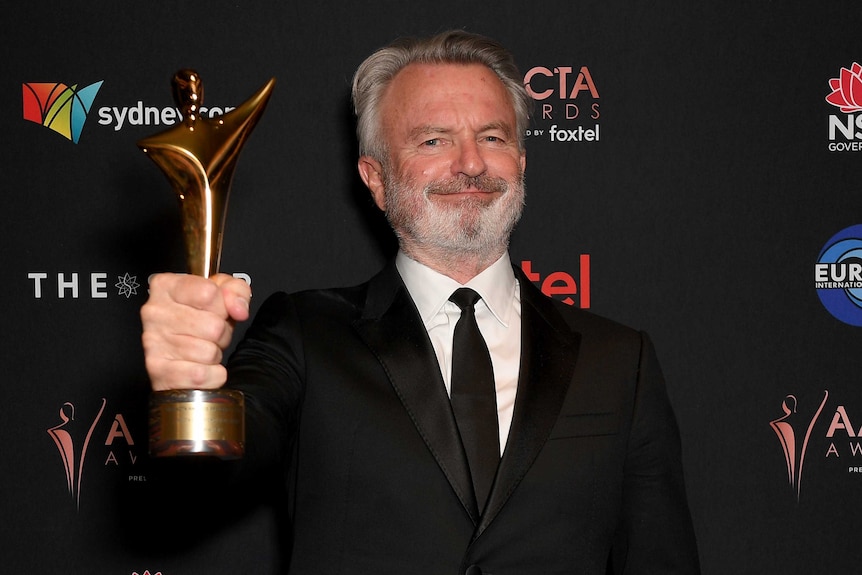 Sam Neill holding an award