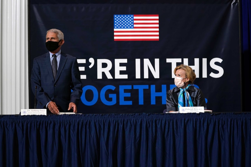 Senior US officials Dr Anthony Fauci and Dr Deborah Birx stand in front of a banner reading "we're in this together".