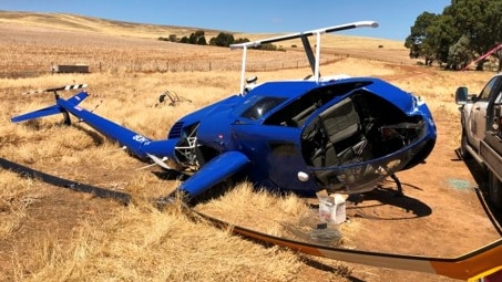 A blue helicopter crashed on its side on brown grass. 
