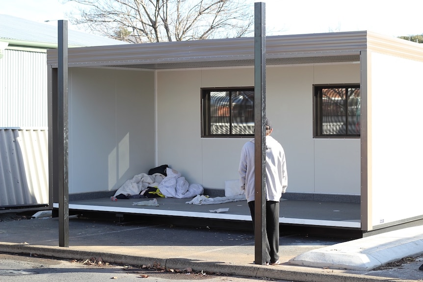 A man stands facing an unfurnished shelter for homeless people.