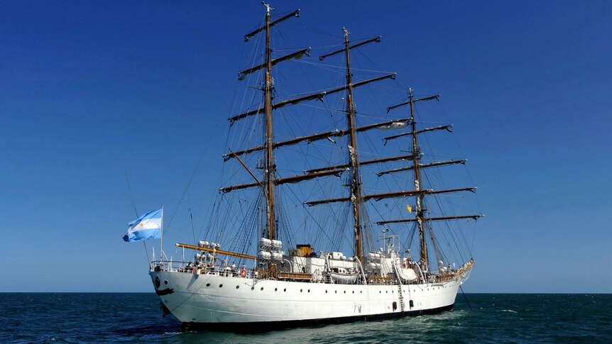 A tall sailing ship bearing Argentina's light blue and white flag at sea on a sunny day