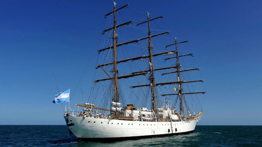 A tall sailing ship bearing Argentina's light blue and white flag at sea on a sunny day