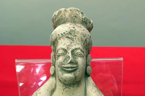 A historic stone artefact of a woman is placed on a red background