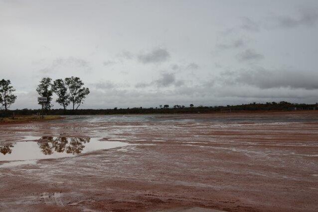 A wide shot of a foggy sky and wet, red dirt ground