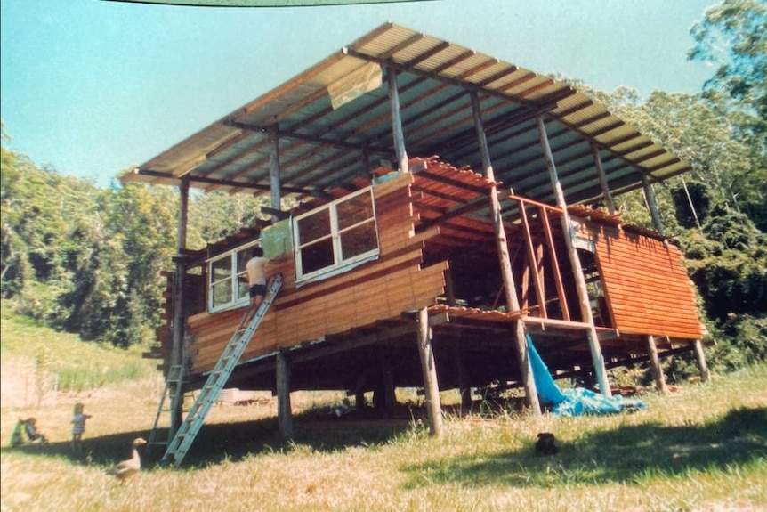 A young David Flinter on a ladder resting on a half-built wooden house.