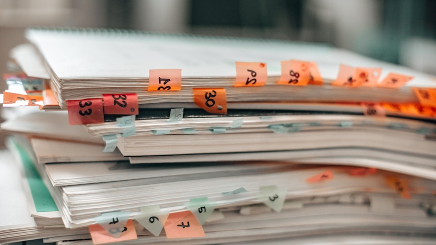 Image of a stack of files holding papers. There are sticky notes with numbers written on them poking out. 
