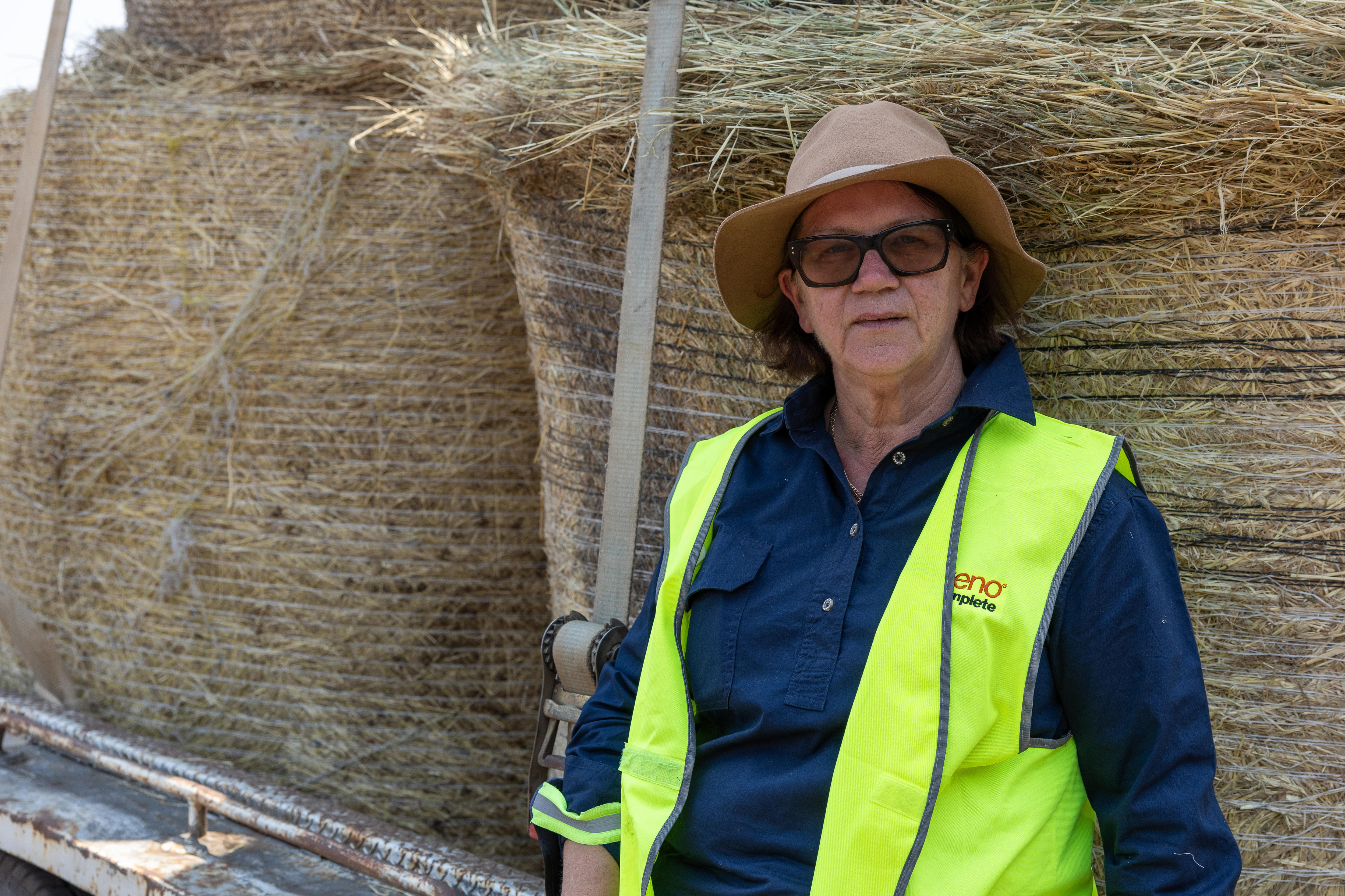 Una mujer con gafas de sol y chaleco de seguridad se encuentra frente a un pajar.