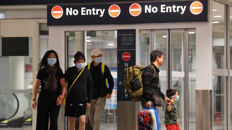 A group of people including men, women and small children with face masks on walking in an airport.