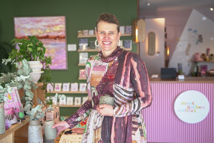 A woman with short hair stands in a colourful store full of homewares.