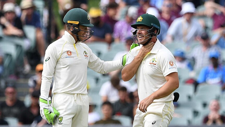 Australian cricketer Tim Paine pats Aaron Finch on the shoulder as Finch holds his throat.