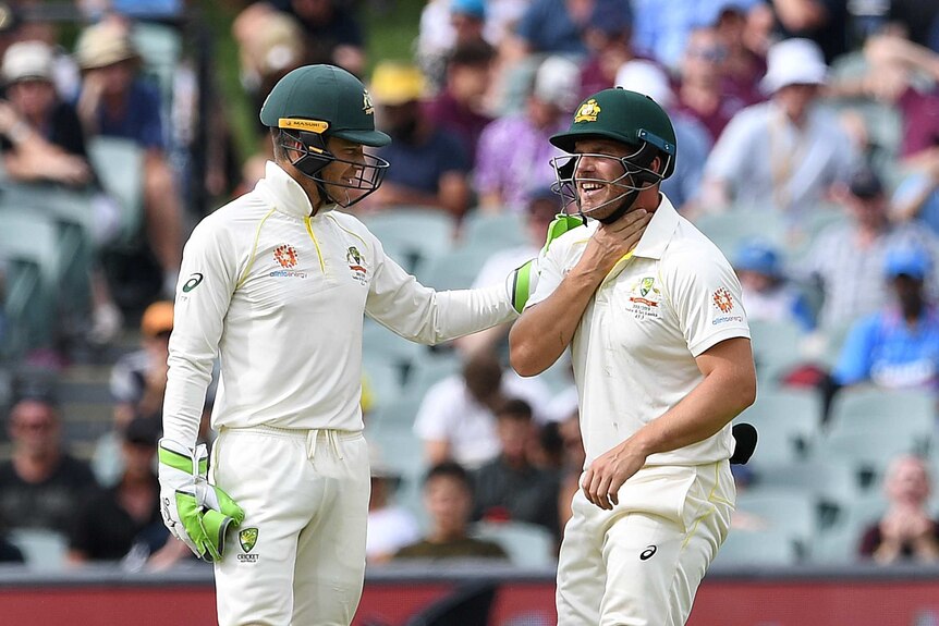 Australian cricketer Tim Paine pats Aaron Finch on the shoulder as Finch holds his throat.