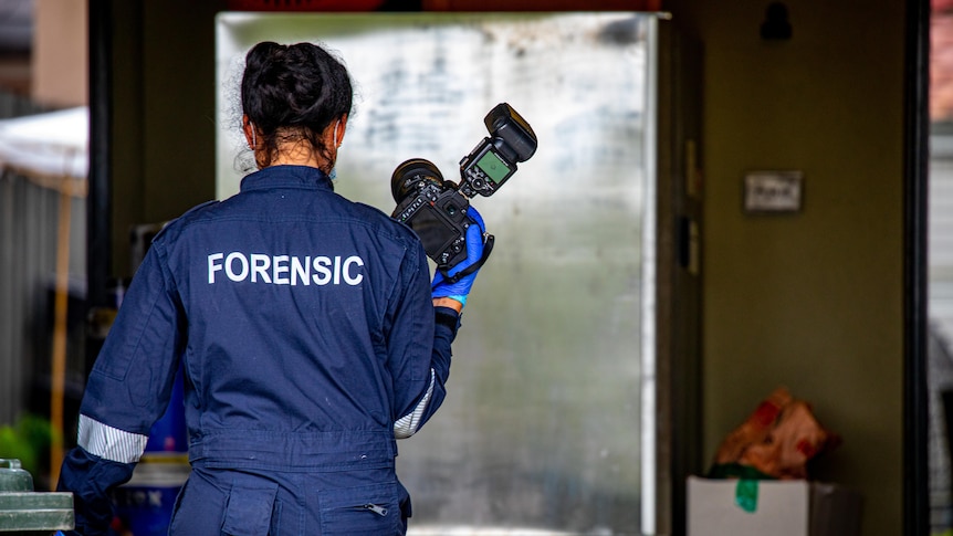 a woman holding a camera wearing a uniform that says "forensic" across the back.