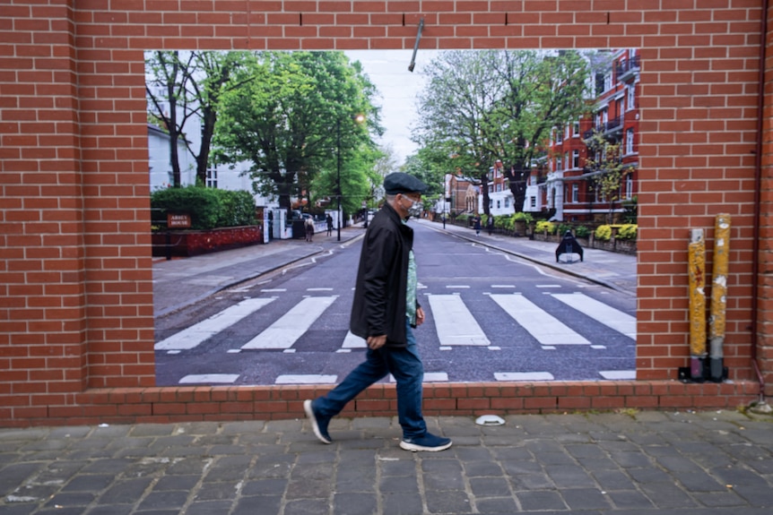 A man walks in front of a photo of Abbey Road similar to the Beatles' famous album cover.