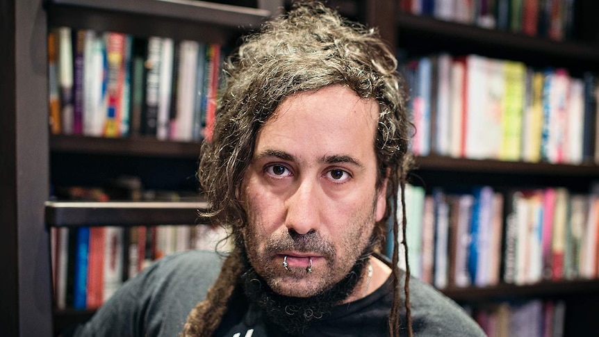 A portrait of Bram Presser standing in front of a bookshelf.