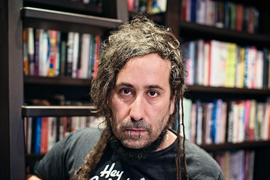 A portrait of Bram Presser standing in front of a bookshelf.