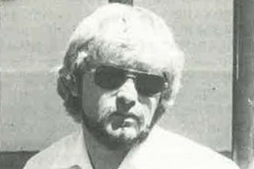 An image of a man with pale hair and aviator-style sunglasses in a white shirt.