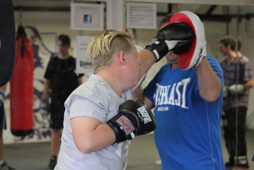 A teenager wearing boxing gloves throws a punch at an instructor in a gymnasium.