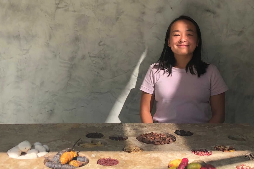 Vicky is sitting at a large concrete table by herself. There is food on the table and she is smiling.