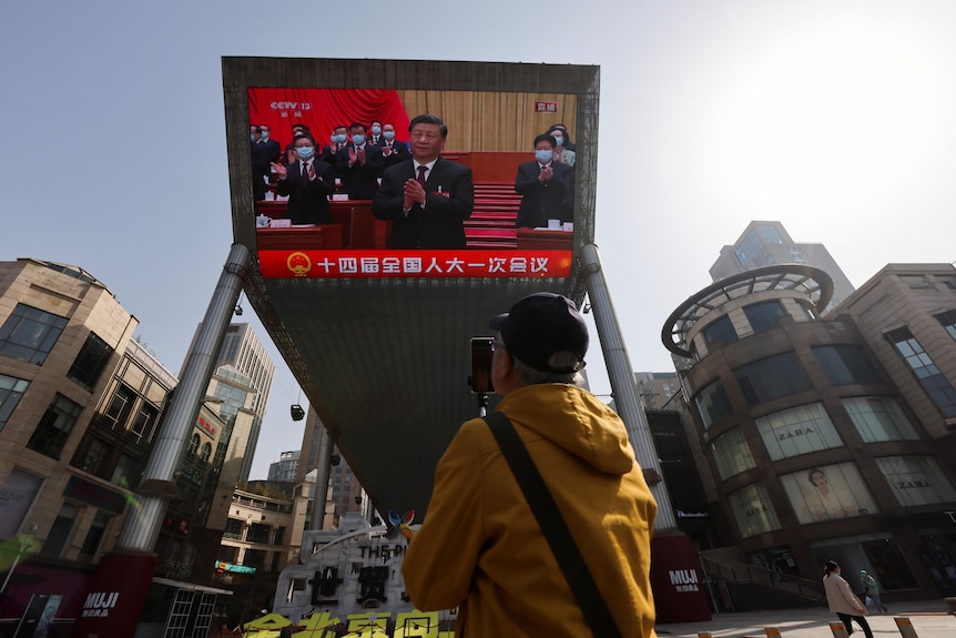 A giant screen displays a live broadcast of Chinese President Xi Jinping.