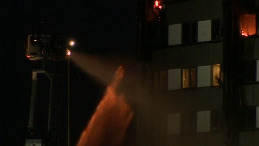 London Fire Brigade personnel spray water on fire at Grenfell Tower as person inside watches on