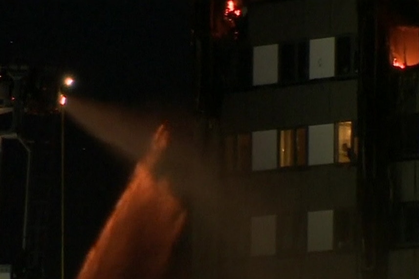 London Fire Brigade personnel spray water on fire at Grenfell Tower as person inside watches on