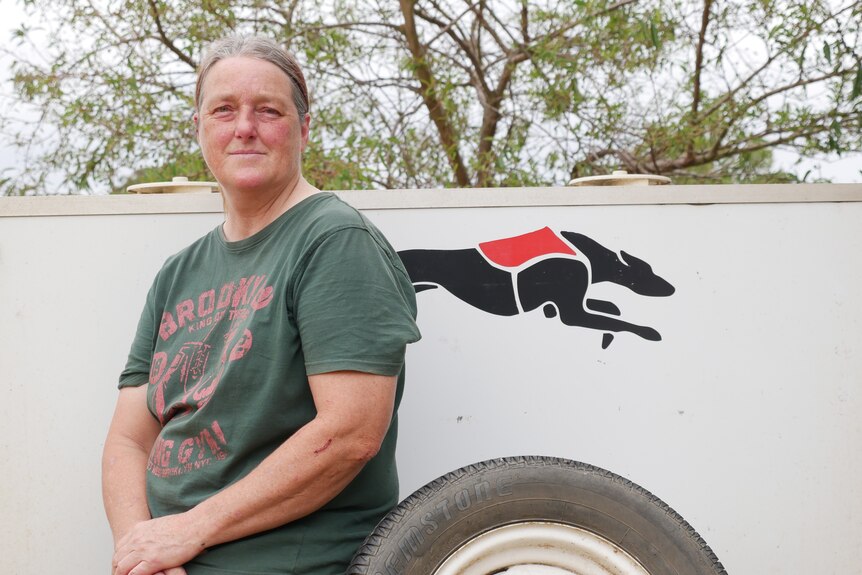 A women in a green shirt sits on a trailer with a logo of a greyhound behind her