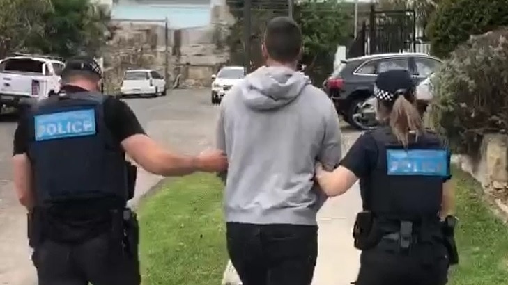 Two police walk up a street linking arms with a man held between them