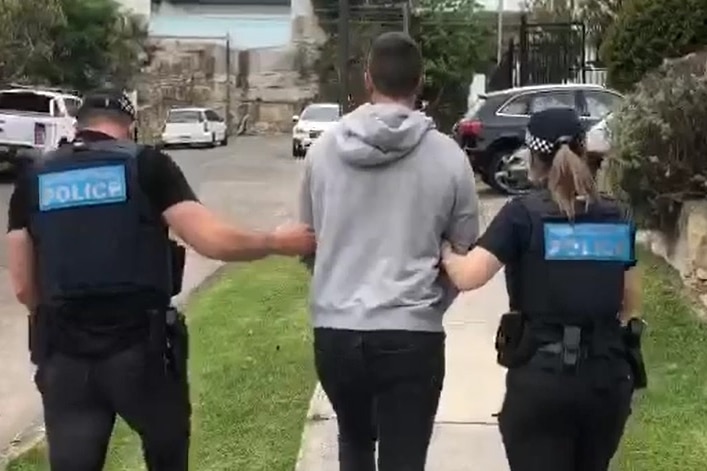 Two police walk up a street linking arms with a man held between them