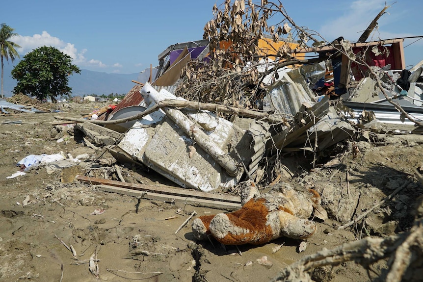 A mud covered teddy bear lies among the a pile of debris on mud