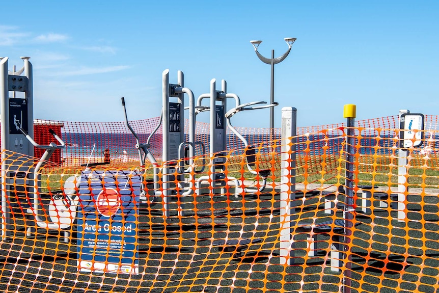 Public exercise equipment cordoned off with orange temporary fencing.