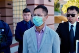 A man in a blue grey suit wearing glasses and a face mask walks