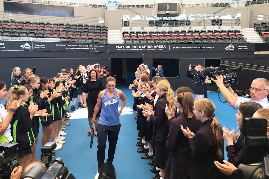 Tennis player Ash Barty is applauded by a crowd at the Queensland Tennis Centre, with Premier Annastacia Palaszczuk following.