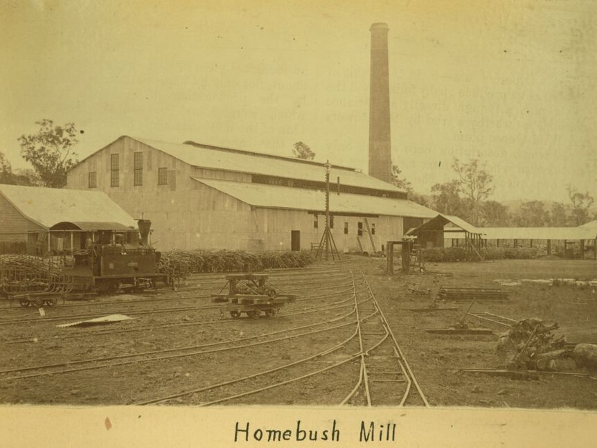 an old image taken of a mill, with a tall chimney stack in the background