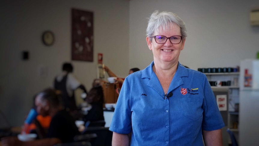 Julie Howard wears a blue Salvation Army shirt and glasses, and smiles at the camera