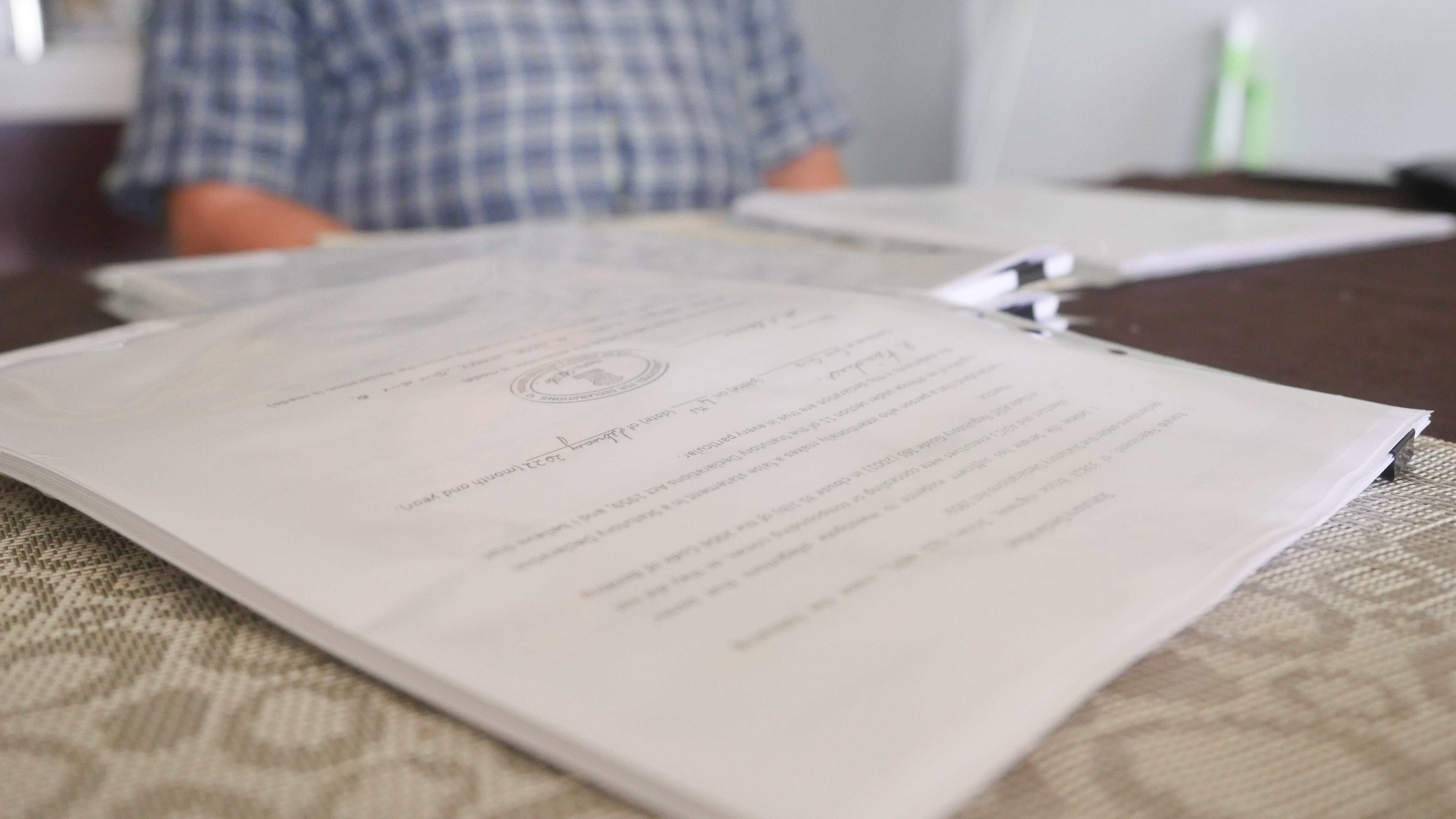 Close up of documents on a table with a blurred figure in the background. 