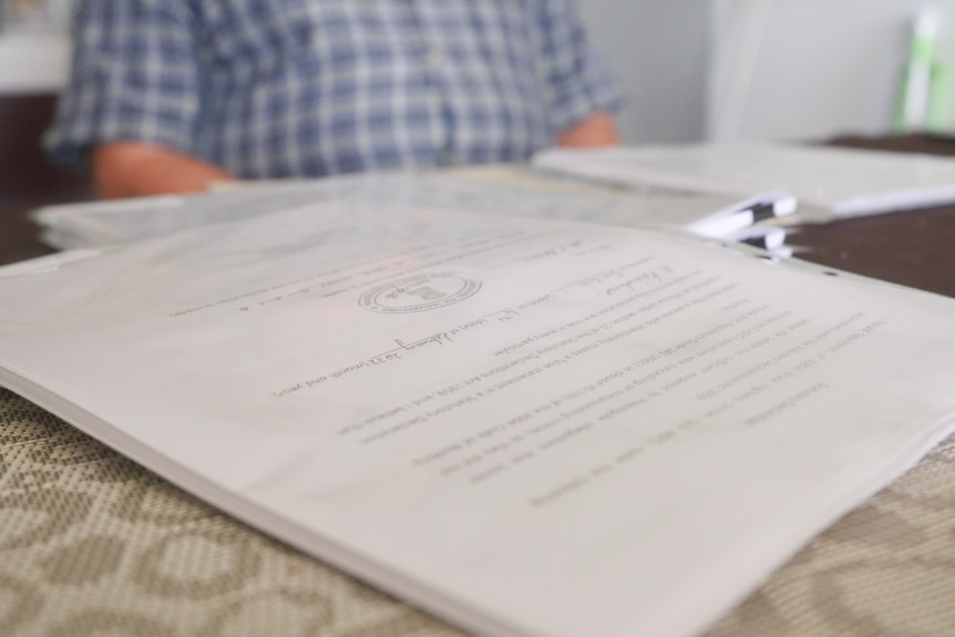 Close up of documents on a table with a blurred figure in the background. 