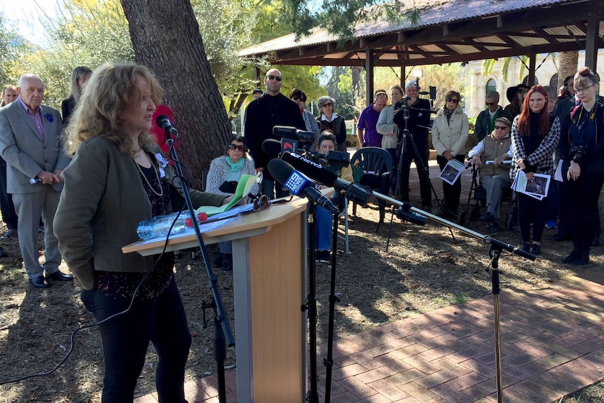 A woman speaks at a lectern to a small crowd of people.