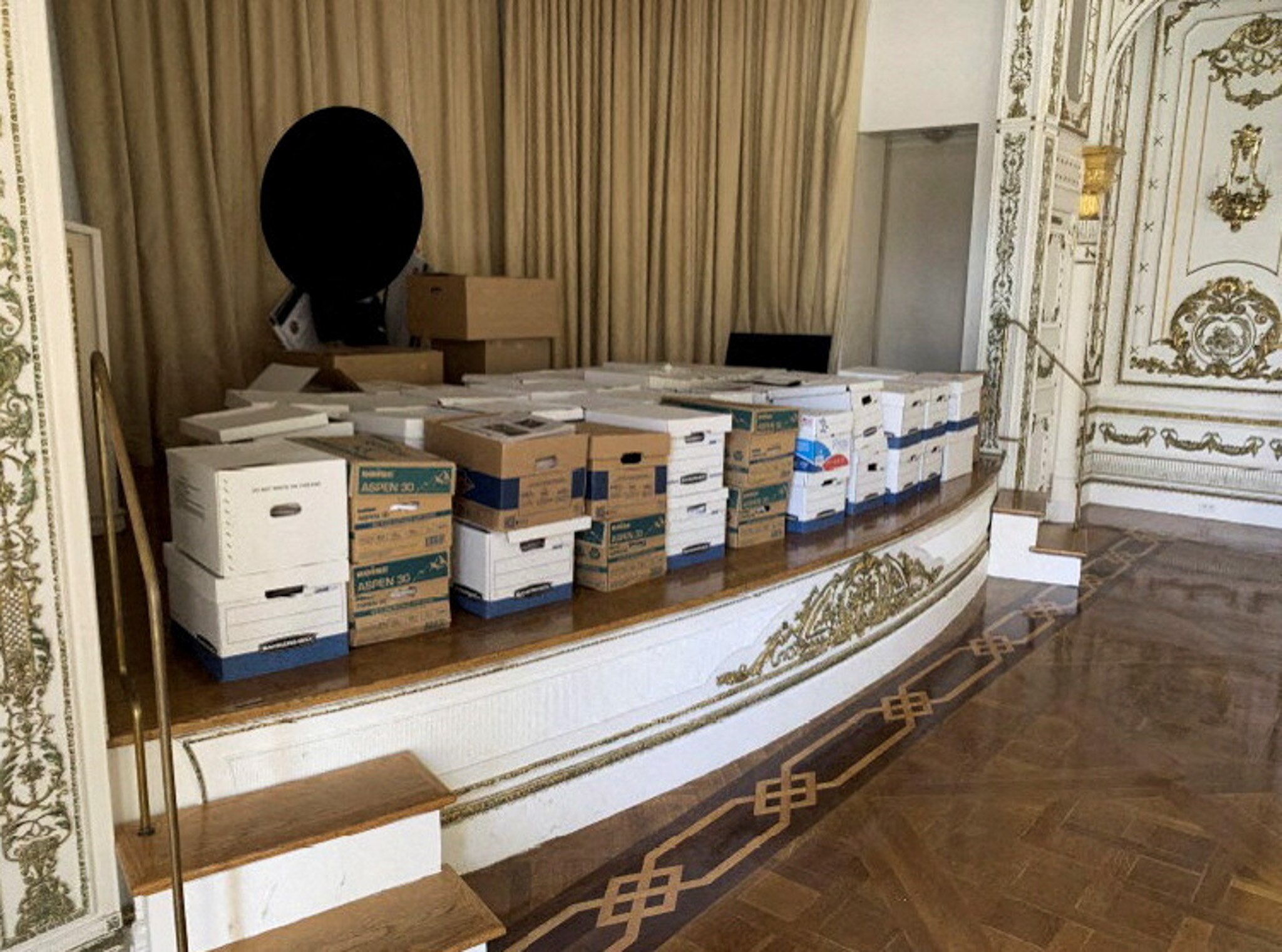 A collection of cardboard boxes sit on a stage inside a ballroom.