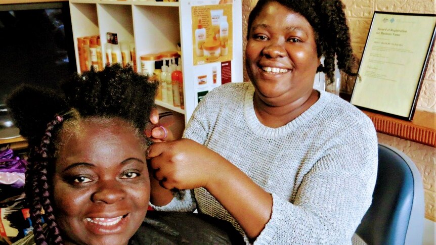 Smiling woman styling another woman's hair at hair salon