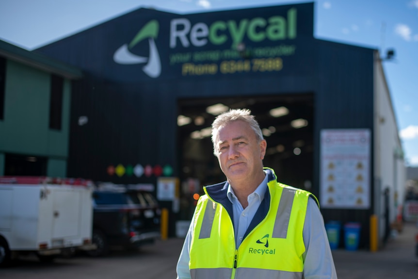 A man in a fluro yellow vest smiles in front of a black building with "Recycal" in green and white  lettering.