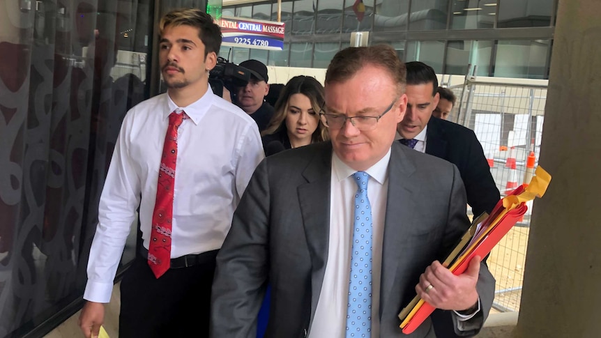 Elijah Taylor is followed by a media pack, walking with his lawyer outside the court.