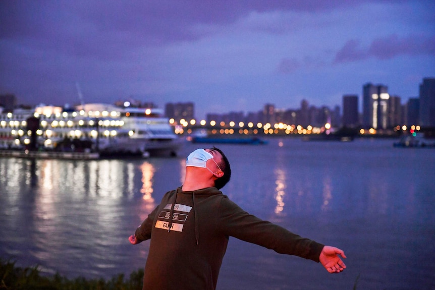 A man in a face mask with his arms outstretched next to a river