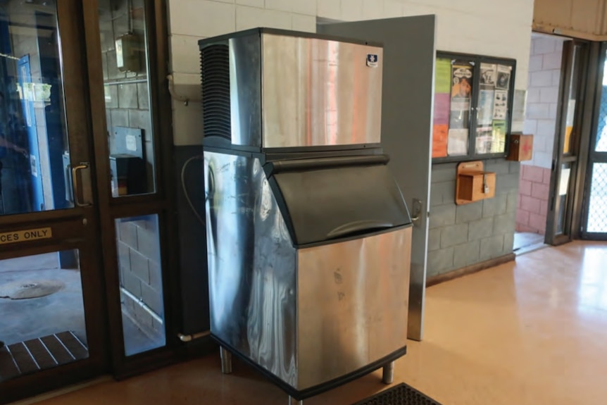 A large stainless steel machine that produces ice positioned against a wall.
