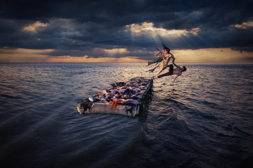 a digitally edited image of dancers on a barge, they appear to be in the middle of the ocean under a cloudy sky