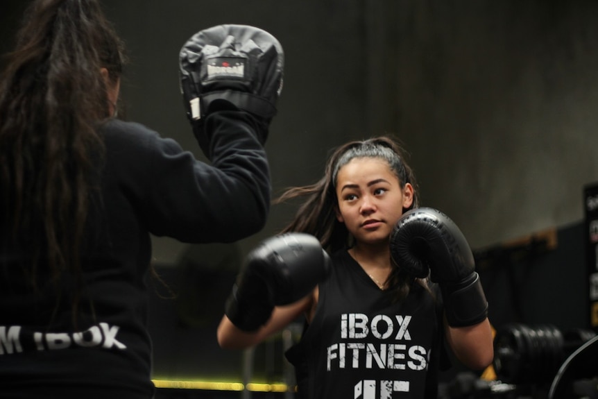 Teya Garcia gets ready to punch a black boxing mit that her sister is holding up.