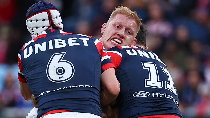 A Cowboys NRL player is tackled by two Roosters opponents.