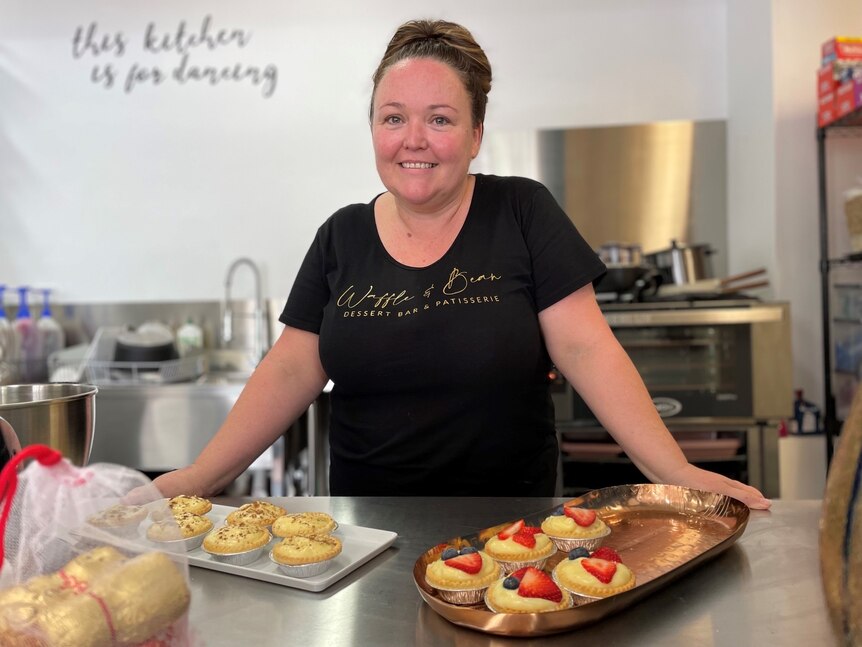 A woman in a black shirt and brown hair standing in commercial kitchen, smiling.