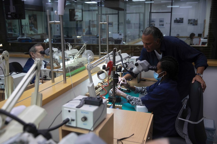 Isaac Levy, owner of Israeli jewelry company Yvel watches over a worker and parts of a mask in a workshop.