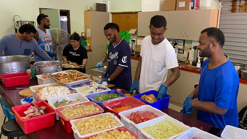 A group of Fijian PALM workers and a pastor chopping food to cook in a kitchen.