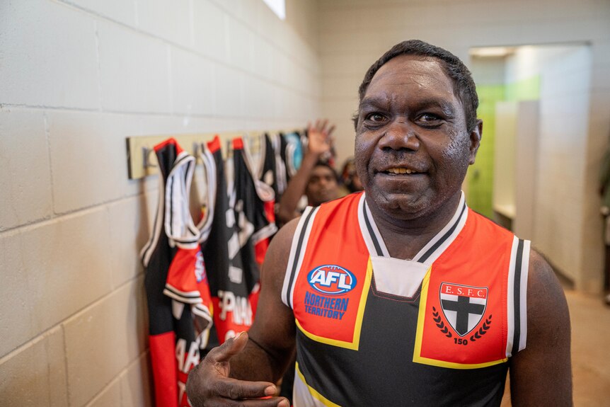 A photo of an Indigenous man wearing a local AFL club jersey standing in club changing room.